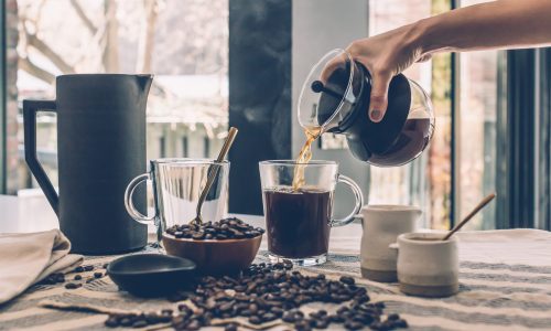 Tafel met Koffie koppen, koffie bonen en hand die vers gezette koffie inschenkt