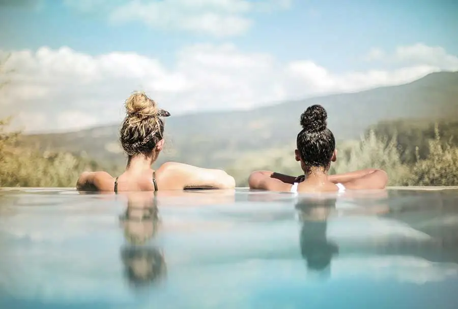 Twee dames relaxen aan zwembadrand uitkijken over de bergen