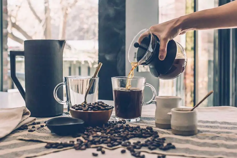 Tafel met Koffie koppen, koffie bonen en hand die vers gezette koffie inschenkt